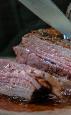 person slicing juicy medium rare meat on top of brown wooden cutting board